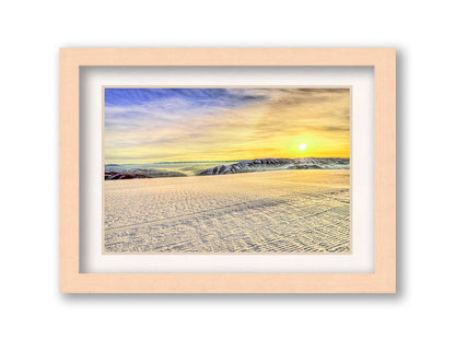 A photo of the sunrise over Sundance Ski Resort. The sun creates a yellow reflective glow on the freshly groomed ski slope. Printed on paper, matted, and framed.