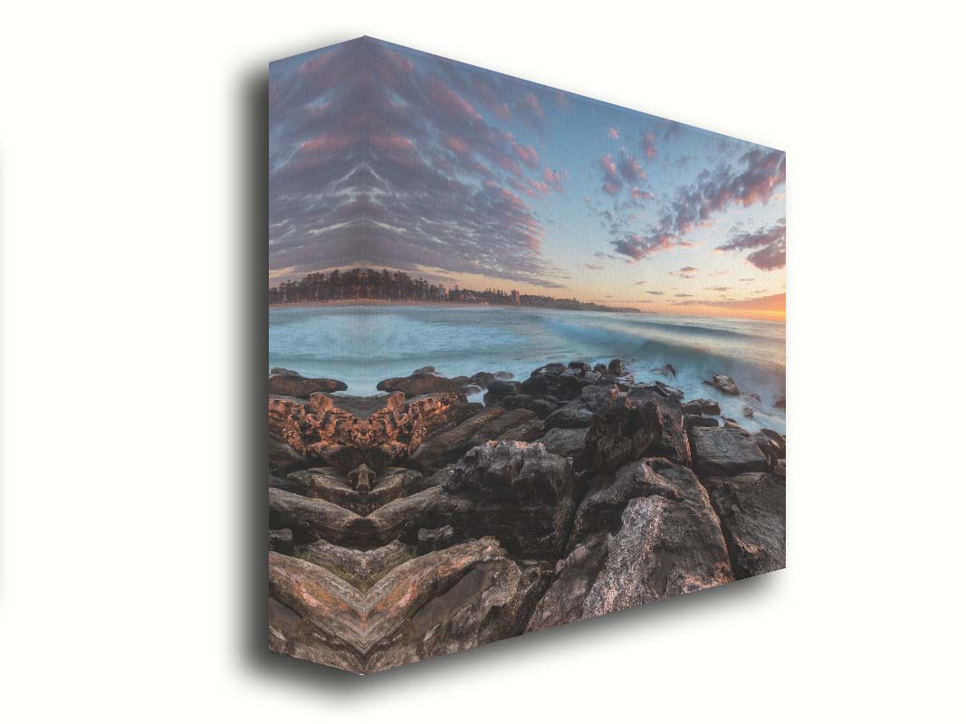 A photo of the sunrise at Manly Beach in Sydney, Australia. The city sits in the background as waves roll against the rocks. Printed on canvas.