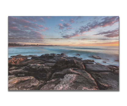 A photo of the sunrise at Manly Beach in Sydney, Australia. The city sits in the background as waves roll against the rocks. Printed on a box board.