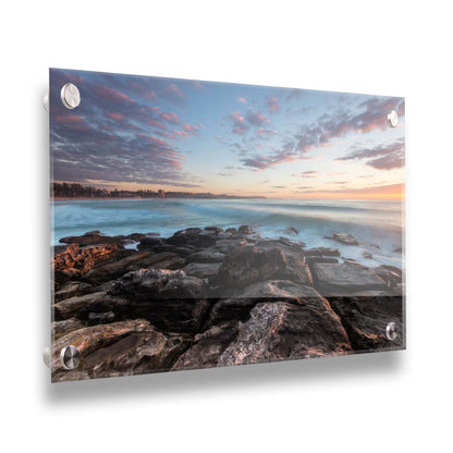 A photo of the sunrise at Manly Beach in Sydney, Australia. The city sits in the background as waves roll against the rocks. Printed on acrylic.