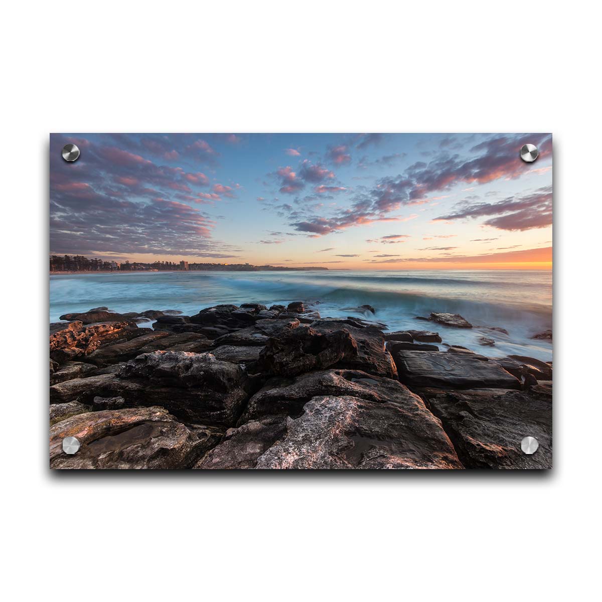 A photo of the sunrise at Manly Beach in Sydney, Australia. The city sits in the background as waves roll against the rocks. Printed on acrylic.