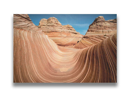 A photo of the "Wave" rock formation at Coyote Buttes North in Utah. The wavy sandstone layers create rolling waves where they have been carved out of the mountainside. The orange hues of the stone are sharply contrasted by the vibrant blue of the sky. Printed on canvas.