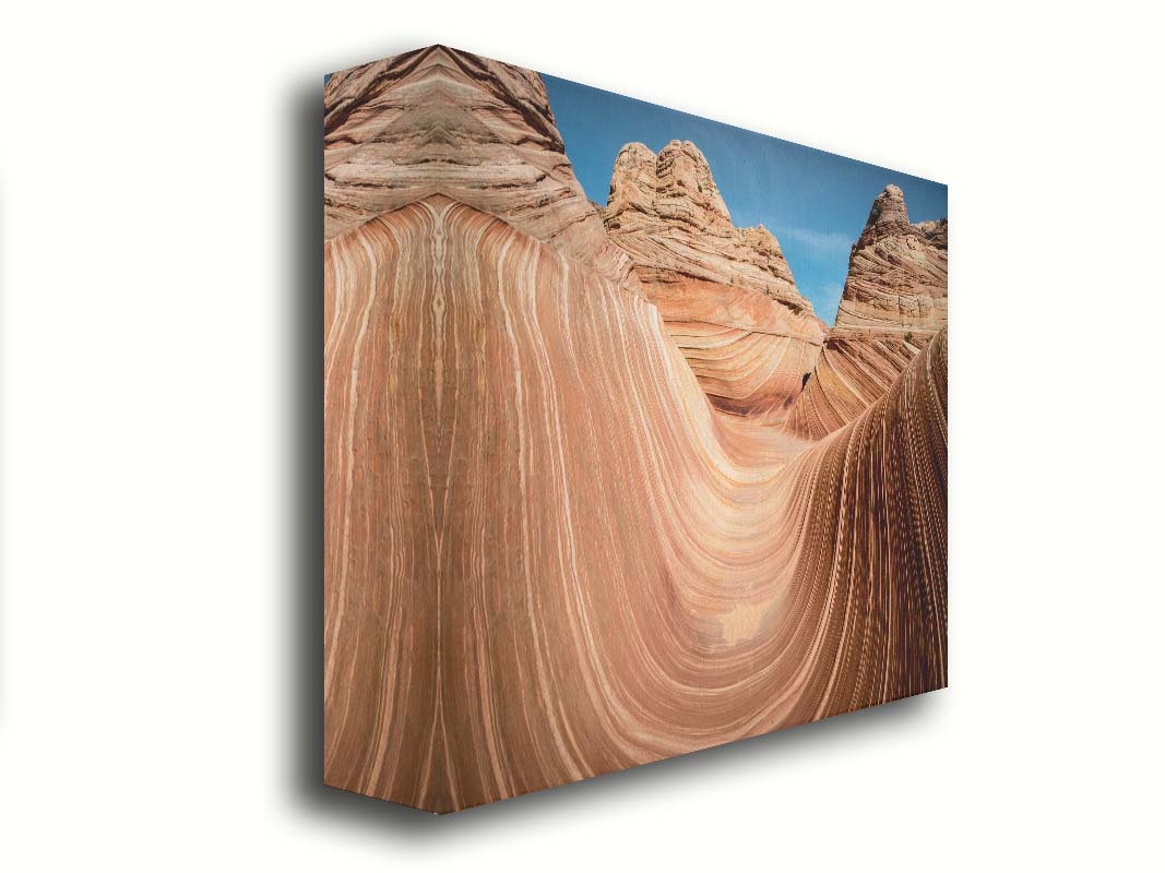 A photo of the "Wave" rock formation at Coyote Buttes North in Utah. The wavy sandstone layers create rolling waves where they have been carved out of the mountainside. The orange hues of the stone are sharply contrasted by the vibrant blue of the sky. Printed on canvas.