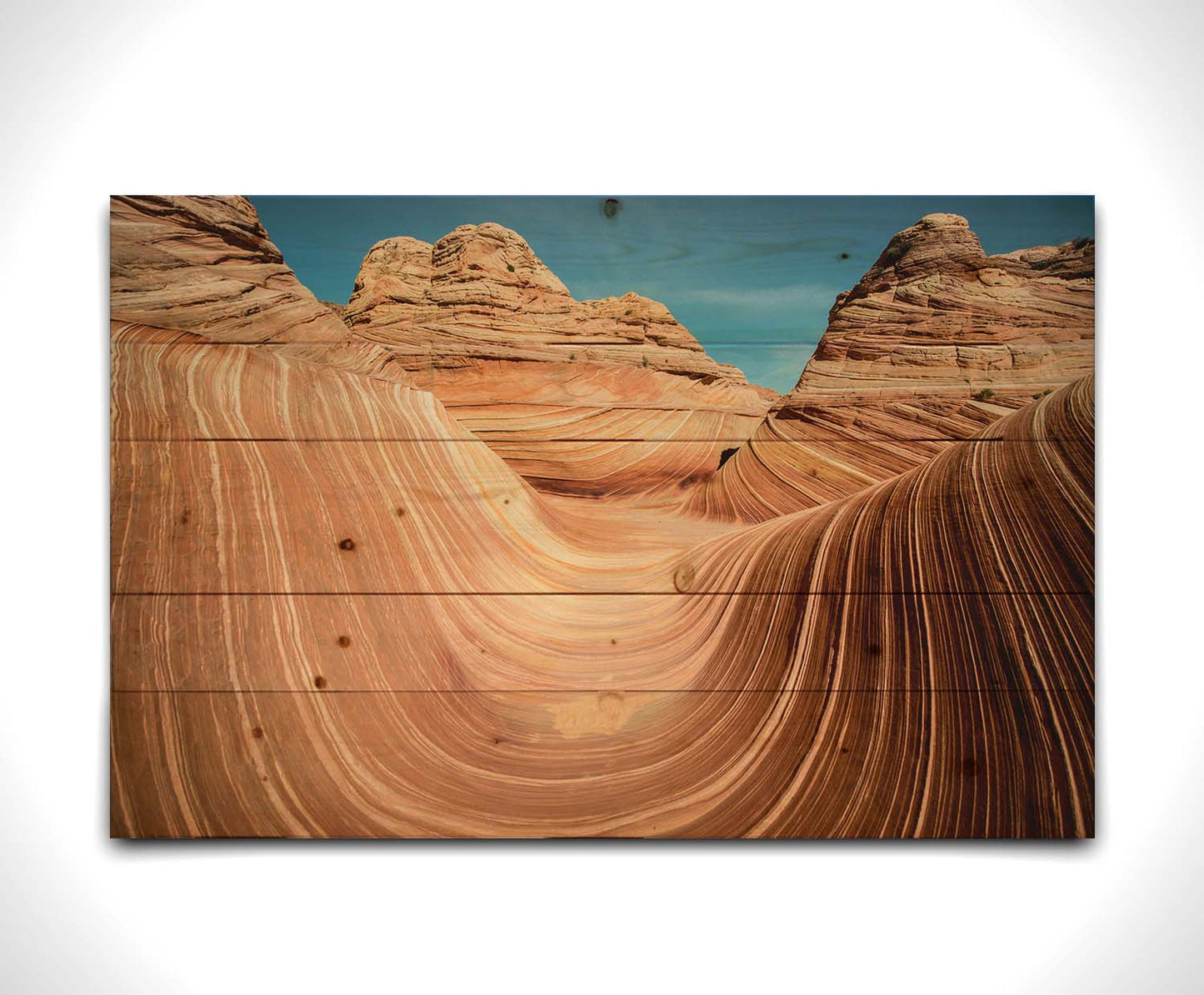 A photo of the "Wave" rock formation at Coyote Buttes North in Utah. The wavy sandstone layers create rolling waves where they have been carved out of the mountainside. The orange hues of the stone are sharply contrasted by the vibrant blue of the sky. Printed on a wood pallet.