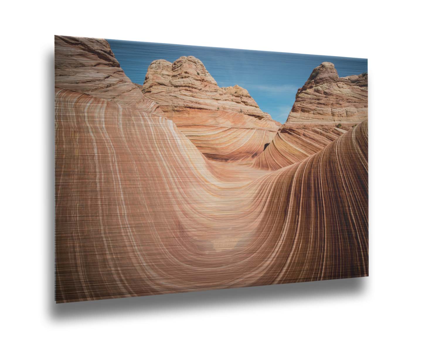 A photo of the "Wave" rock formation at Coyote Buttes North in Utah. The wavy sandstone layers create rolling waves where they have been carved out of the mountainside. The orange hues of the stone are sharply contrasted by the vibrant blue of the sky. Printed on metal.