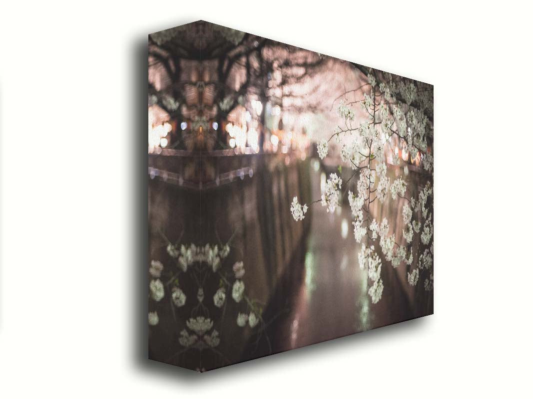 A closeup photo of a branch of cherry blossoms, hanging over the Meguro River. Out of focus in the background, the river reflects twinkles of the city lights. Printed on canvas.