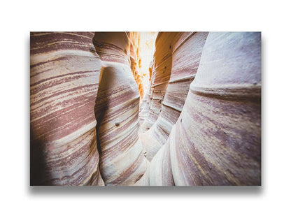 A photo of Zebra Slot Canyon in Escalante National Monument, Utah. A tight formation of alternating, red and white striped stone walls wave into the distance, where yellow light can be seen. Printed on canvas.