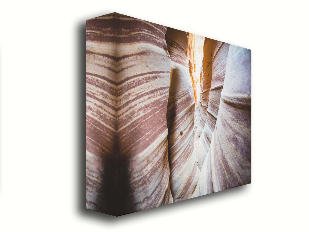 A photo of Zebra Slot Canyon in Escalante National Monument, Utah. A tight formation of alternating, red and white striped stone walls wave into the distance, where yellow light can be seen. Printed on canvas.