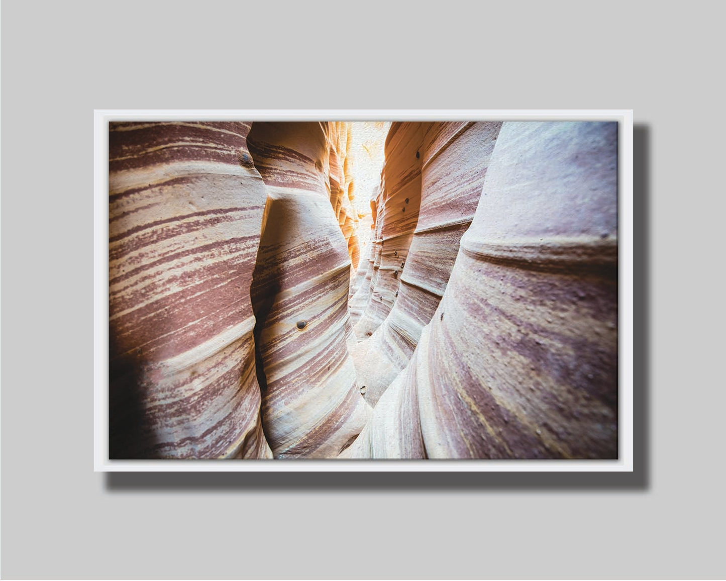 A photo of Zebra Slot Canyon in Escalante National Monument, Utah. A tight formation of alternating, red and white striped stone walls wave into the distance, where yellow light can be seen. Printed on canvas in a float frame.