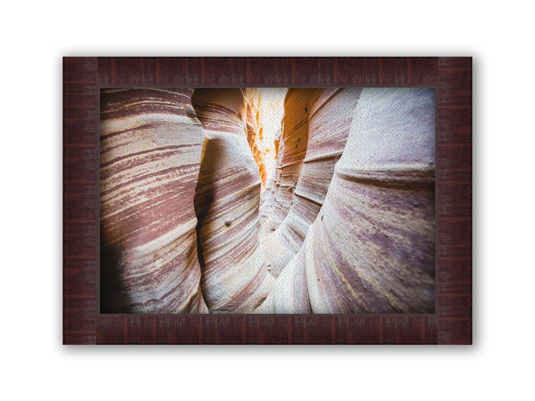 A photo of Zebra Slot Canyon in Escalante National Monument, Utah. A tight formation of alternating, red and white striped stone walls wave into the distance, where yellow light can be seen. Printed on canvas and framed.