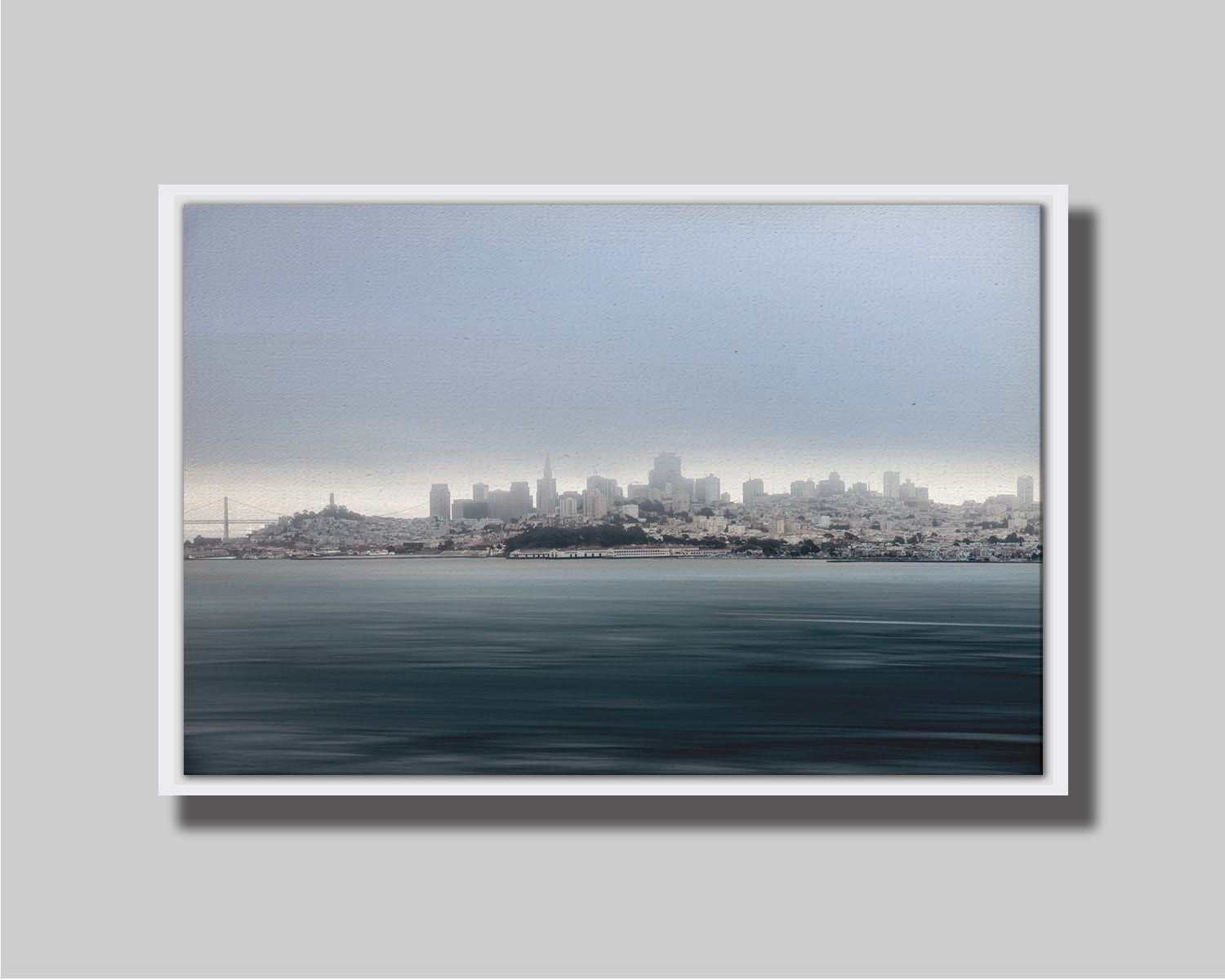 A photo of San Francisco bay taken from Vista Point. The long exposure of the photo creates a smoothing effect on the dark waters, and a heavy cloud of fog site just across the top of the city on the horizon. Printed on canvas in a float frame.