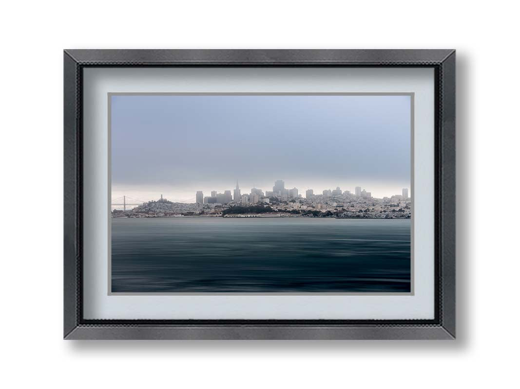 A photo of San Francisco bay taken from Vista Point. The long exposure of the photo creates a smoothing effect on the dark waters, and a heavy cloud of fog site just across the top of the city on the horizon. Printed on paper, matted, and framed.