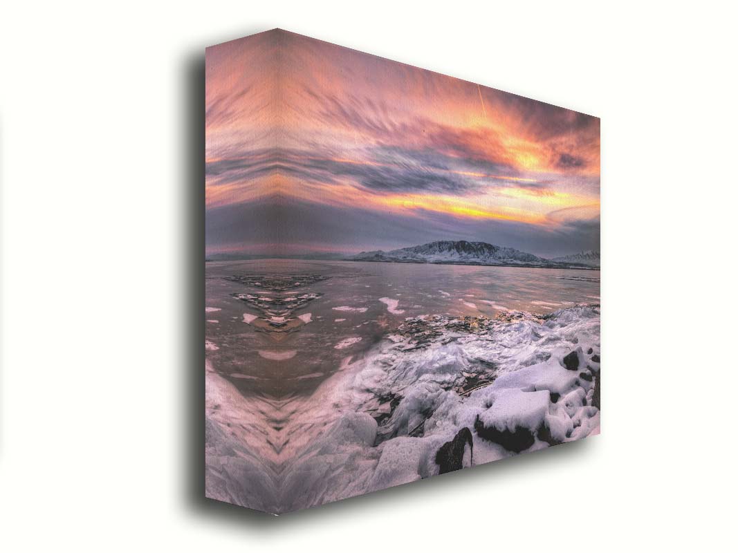 A photo of the sun setting at Mount Timpanogos, Utah, one Christmas evening. Its golden light can be seen peeking through the clouds across the horizon of a frozen lake, wind pushing thin sheets of ice up onto the shore. Printed on canvas.