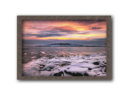 A photo of the sun setting at Mount Timpanogos, Utah, one Christmas evening. Its golden light can be seen peeking through the clouds across the horizon of a frozen lake, wind pushing thin sheets of ice up onto the shore. Printed on canvas and framed.