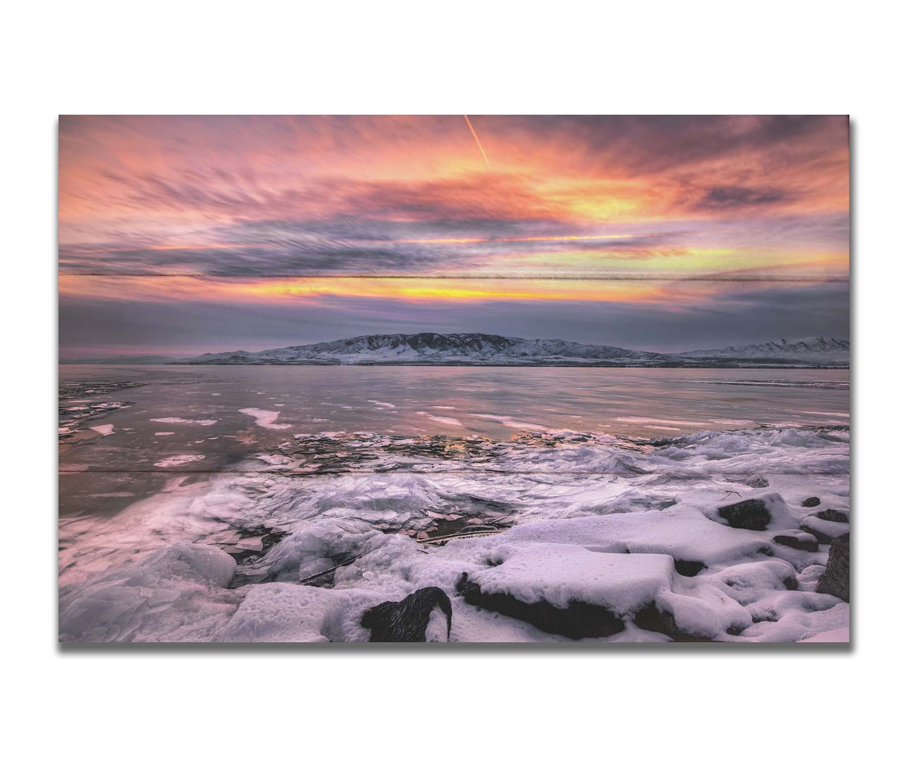 A photo of the sun setting at Mount Timpanogos, Utah, one Christmas evening. Its golden light can be seen peeking through the clouds across the horizon of a frozen lake, wind pushing thin sheets of ice up onto the shore. Printed on a box board.