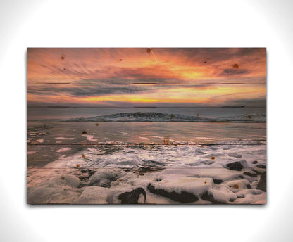 A photo of the sun setting at Mount Timpanogos, Utah, one Christmas evening. Its golden light can be seen peeking through the clouds across the horizon of a frozen lake, wind pushing thin sheets of ice up onto the shore. Printed on a wood pallet.