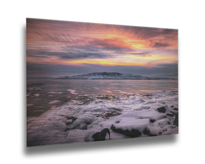 A photo of the sun setting at Mount Timpanogos, Utah, one Christmas evening. Its golden light can be seen peeking through the clouds across the horizon of a frozen lake, wind pushing thin sheets of ice up onto the shore. Printed on metal.