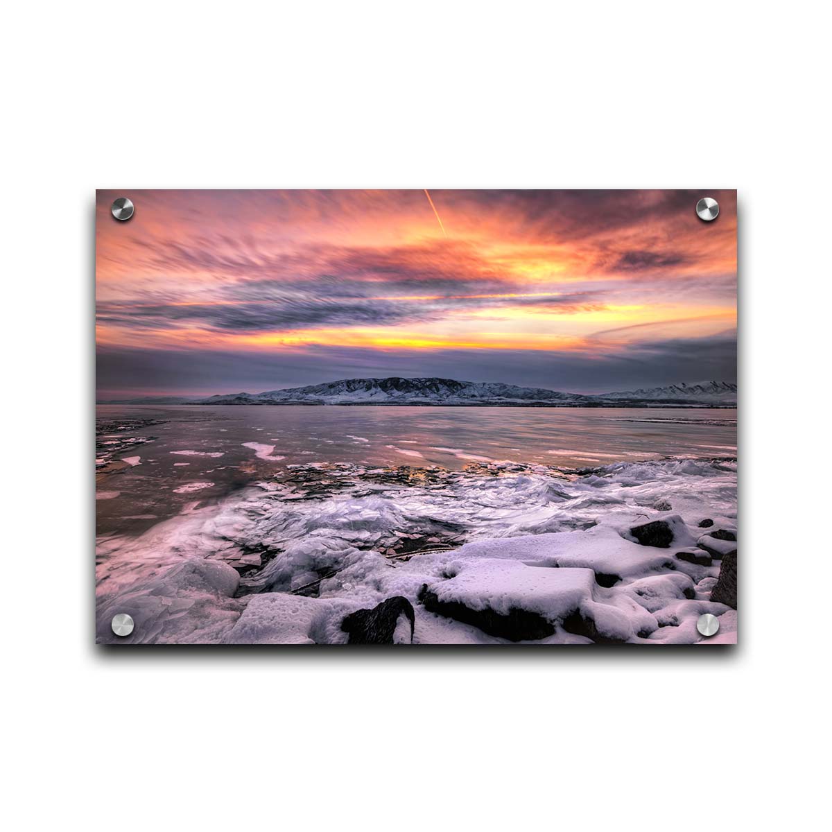 A photo of the sun setting at Mount Timpanogos, Utah, one Christmas evening. Its golden light can be seen peeking through the clouds across the horizon of a frozen lake, wind pushing thin sheets of ice up onto the shore. Printed on acrylic.