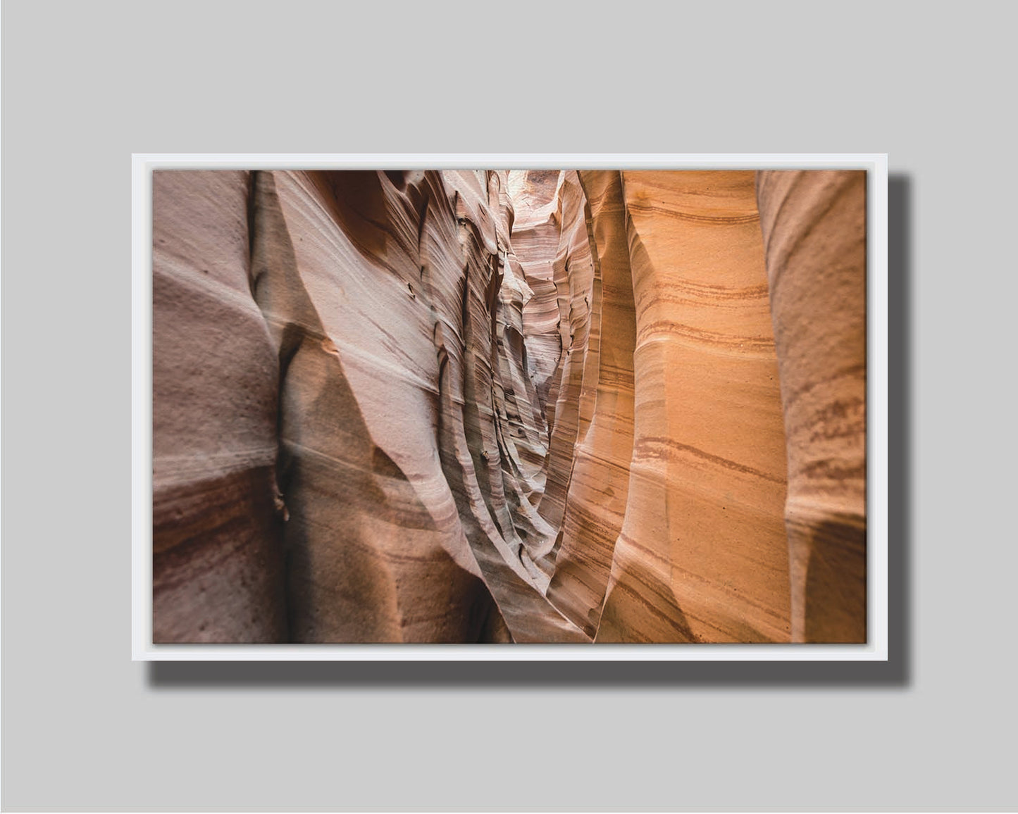 A photo of the Zebra Slot Canyon at Grand Staircase-Escalante National Monument, Utah. The red and orange sandstone stripes alternate in sharp waves down the length of the narrow passageway. Printed on canvas in a float frame.