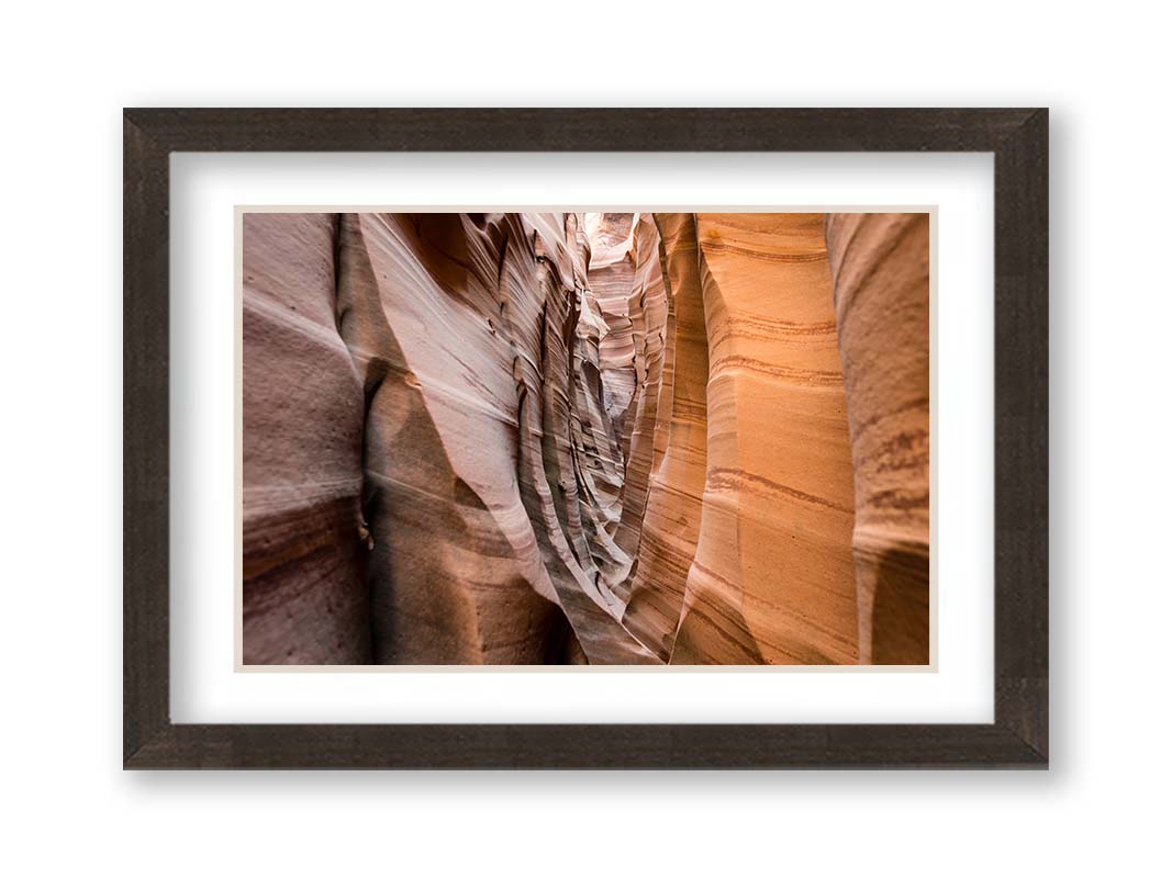 A photo of the Zebra Slot Canyon at Grand Staircase-Escalante National Monument, Utah. The red and orange sandstone stripes alternate in sharp waves down the length of the narrow passageway. Printed on paper, matted, and framed.