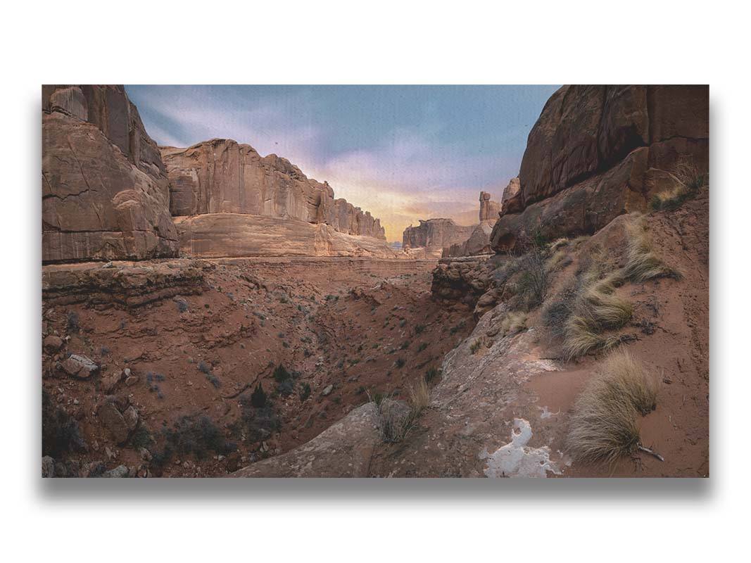 A photo from a Moab, Utah canyon. Sparse shrubbery is scattered along the canyon surrounded by sandstone walls. Printed on canvas.