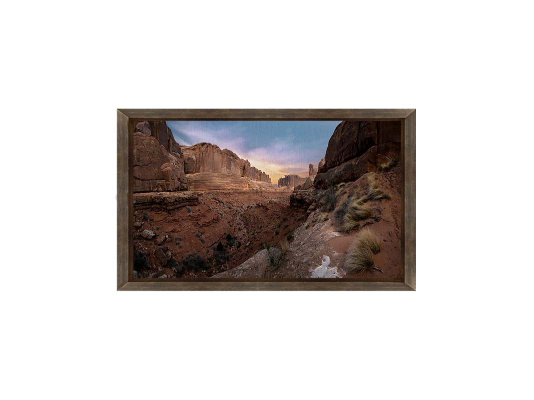 A photo from a Moab, Utah canyon. Sparse shrubbery is scattered along the canyon surrounded by sandstone walls. Printed on canvas and framed.