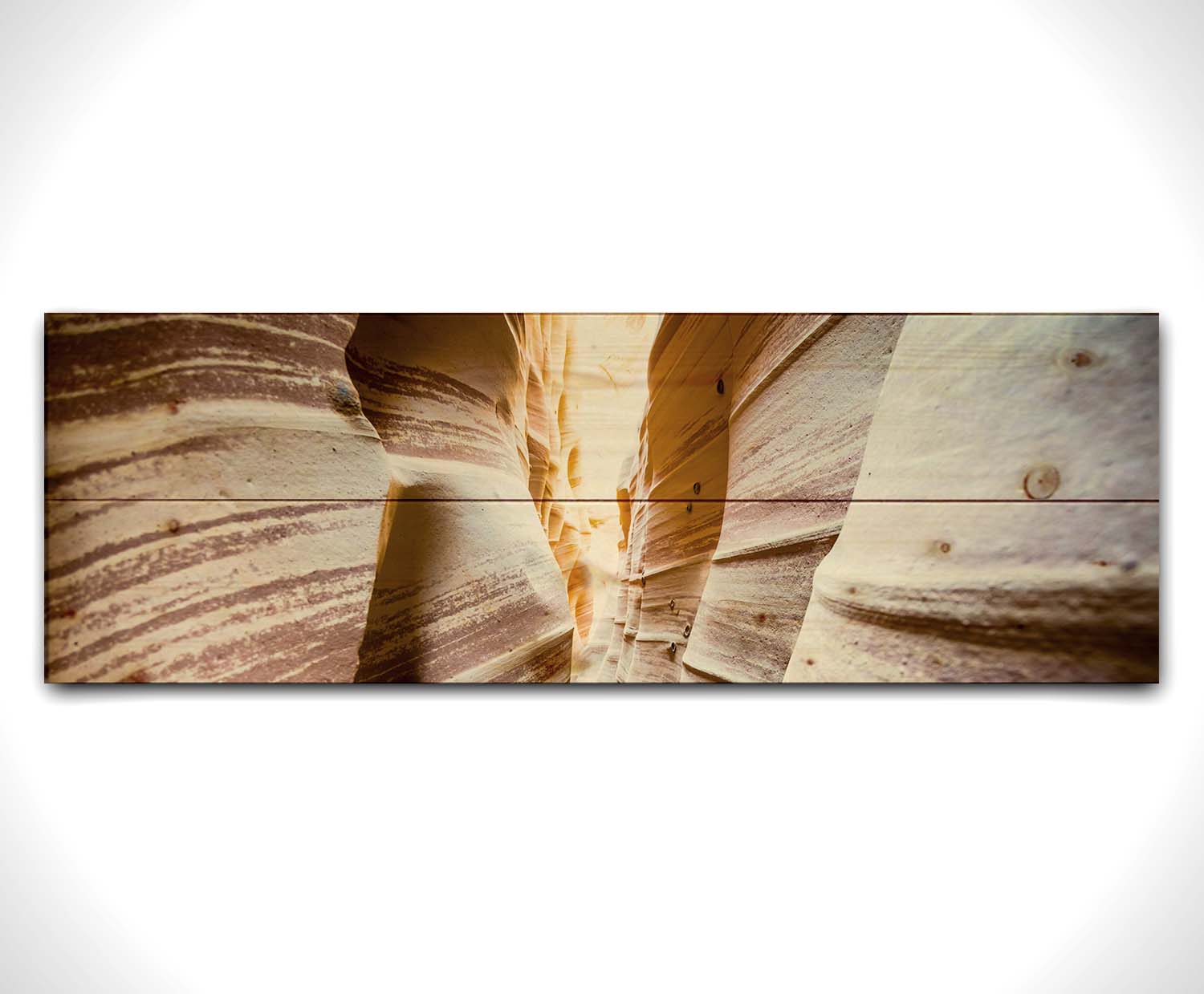 A photo looking down a narrow slot canyon. The walls of sandstone lead out into the light, creating added perspective with their red and white striped layers of stone drawing into the distance. Printed on a wood pallet.