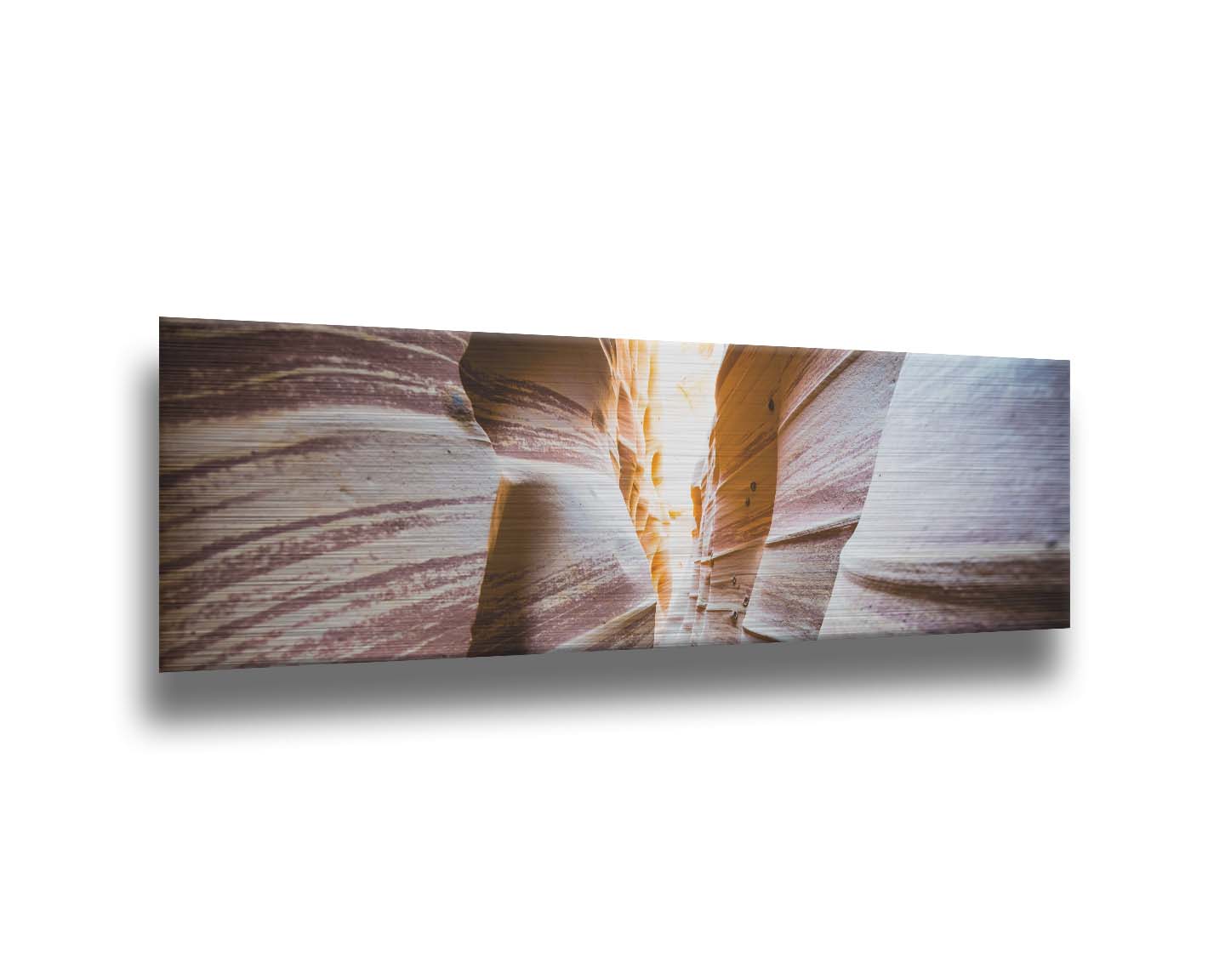 A photo looking down a narrow slot canyon. The walls of sandstone lead out into the light, creating added perspective with their red and white striped layers of stone drawing into the distance. Printed on metal.