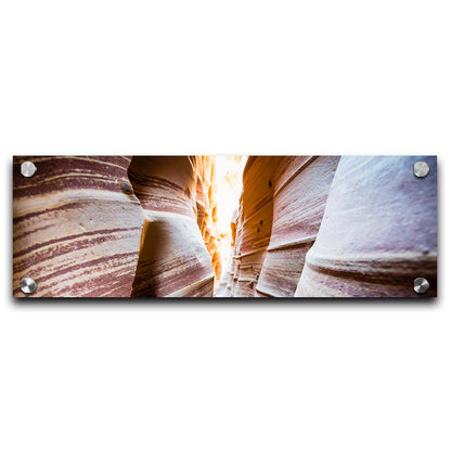 A photo looking down a narrow slot canyon. The walls of sandstone lead out into the light, creating added perspective with their red and white striped layers of stone drawing into the distance. Printed on acrylic.