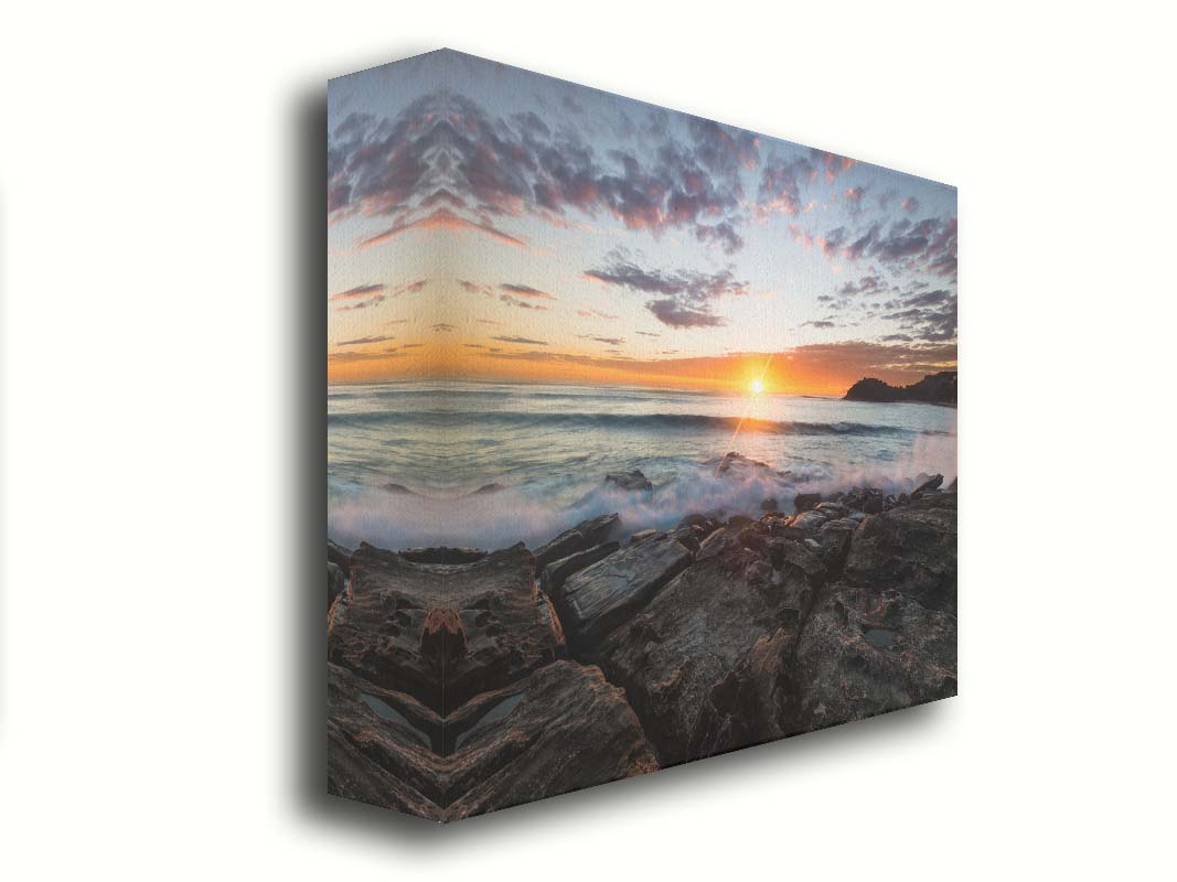 A photo of the sunrise over the ocean horizon at Manly Beach, Sydney, Australia. The sun reflecs brightly off the water as the waves splash against the rocky shore. Printed on canvas.