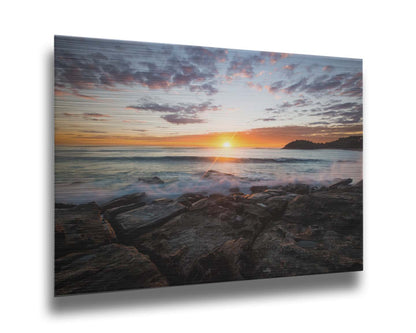 A photo of the sunrise over the ocean horizon at Manly Beach, Sydney, Australia. The sun reflecs brightly off the water as the waves splash against the rocky shore. Printed on metal.