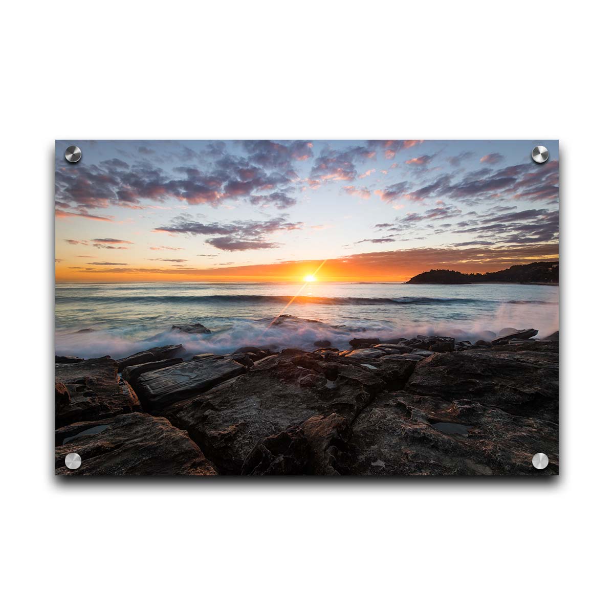 A photo of the sunrise over the ocean horizon at Manly Beach, Sydney, Australia. The sun reflecs brightly off the water as the waves splash against the rocky shore. Printed on acrylic.