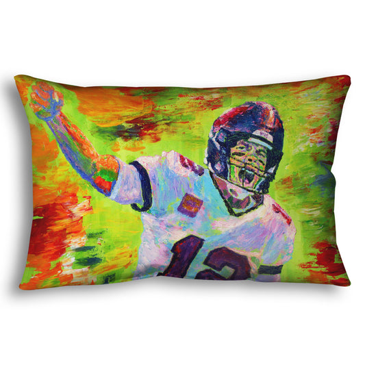 A throw pillow designed with a painting of American football player Tom Brady yelling with his fist in the air, rallying his teammates. Arbitrary colors and visible brushstrokes add to the energy of this painting, alongside the bright greens, reds, and oranges of the backdrop.