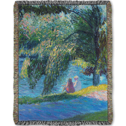 A woven throw blanket designed with a painting of two people sitting by the water, near a park sidewalk, with a large tree above them.
