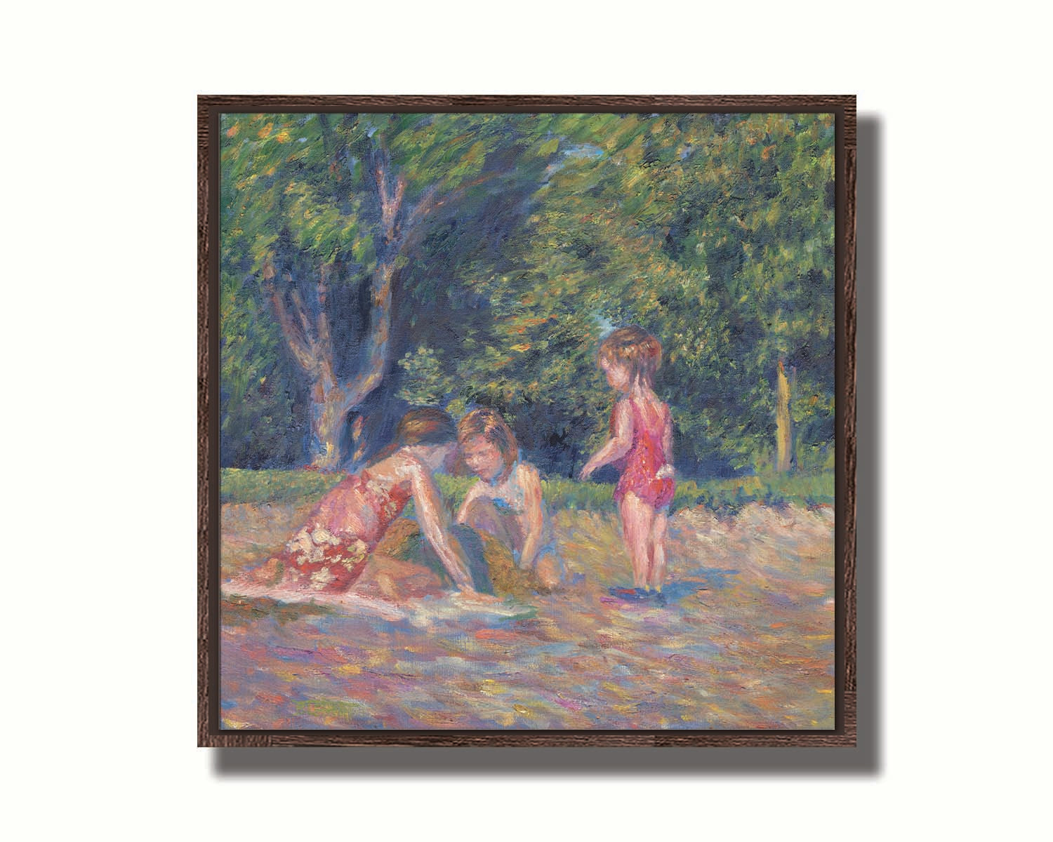 A painting of three children playing in the sand at a beach. Their red swimsuits contrast the green foliage in the background. Printed on canvas in a float frame.