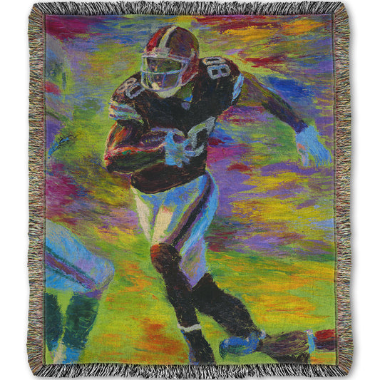 A woven blanket designed with a painting of a football player running across the field with the ball, narrowly avoiding the opposing team's players.