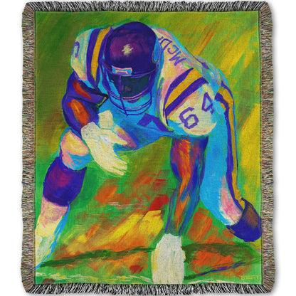 A woven throw blanket designed with a painting of a football player, wearing white and purple, crouched on a bright green field.