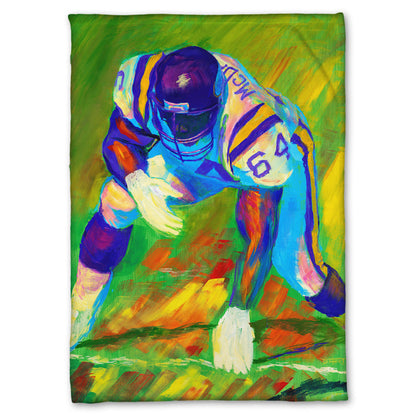 A fleece throw blanket designed with a painting of a football player, wearing white and purple, crouched on a bright green field.