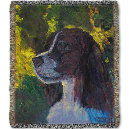 Woven throw blanket designed with a painting of a brown and white spaniel dog, against a background of greens suggesting foliage.