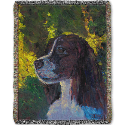 Woven throw blanket designed with a painting of a brown and white spaniel dog, against a background of greens suggesting foliage.