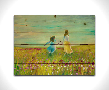 A painting of two people holding hands, walking through a field of green grass peppered with red, pink, and white flowers under a blue sky. Printed on a wood pallet.