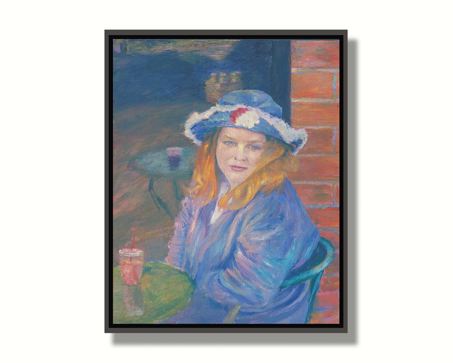 A portrait of a person in a blue outfit, sitting at a table outside a brick building with a drink. Printed on canvas in a float frame.