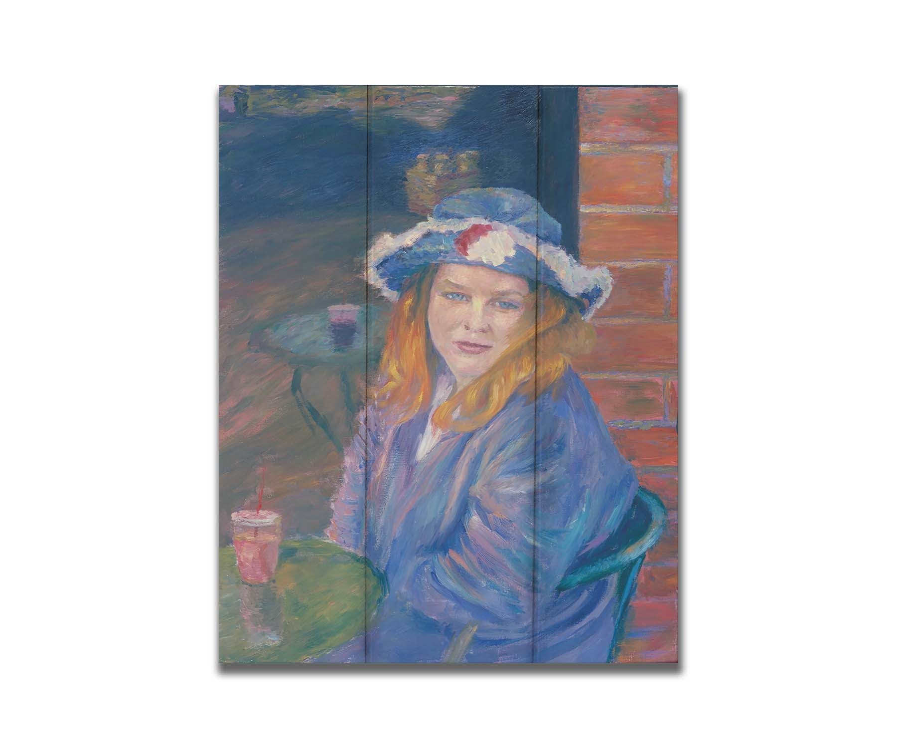 A portrait of a person in a blue outfit, sitting at a table outside a brick building with a drink. Printed on a box board.