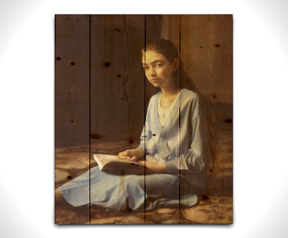 A portrait painting of a young girl dressed in blue and sitting on the floor, reading a book. It is painted in a softly lit, realistic, classical style reminiscent of the Renaissance. Printed on a wood pallet.