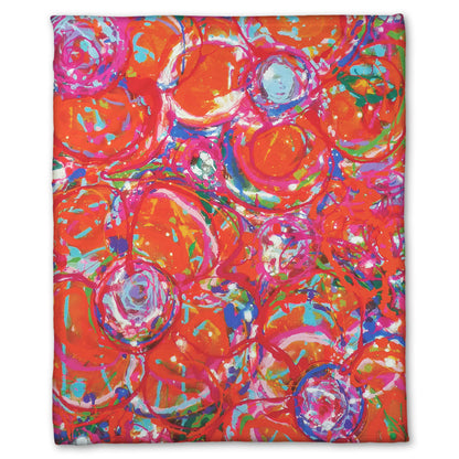 A fleece blanket designed with a drip painting of a cluster of abstracted flowers created with splatters of orange, red, and pink with accents of green, blue, yellow, and purple.