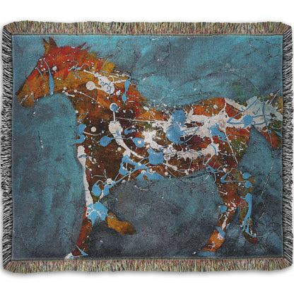A woven throw blanket designed with a drip painting of a brown silhouetted horse accented with blue and white, against a blue background.