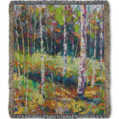 A woven throw blanket designed with a painting of a birch forest in a variety of vibrant colors with textured brushwork.