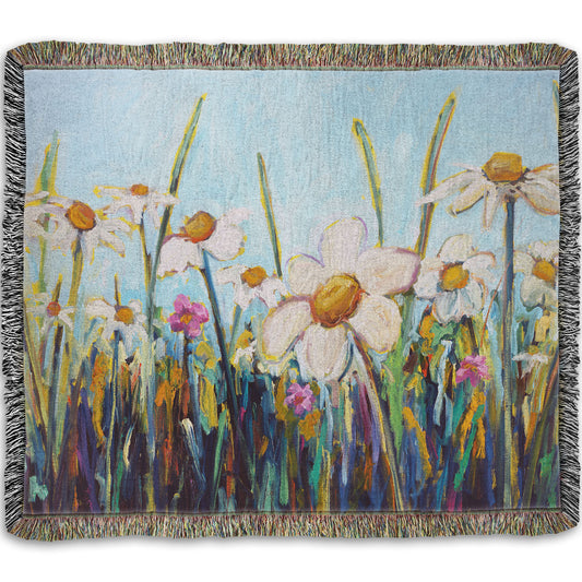 A woven throw blanket designed with a painting of a wildflower field from a low angle, full of white daisies accented by small pink flowers.