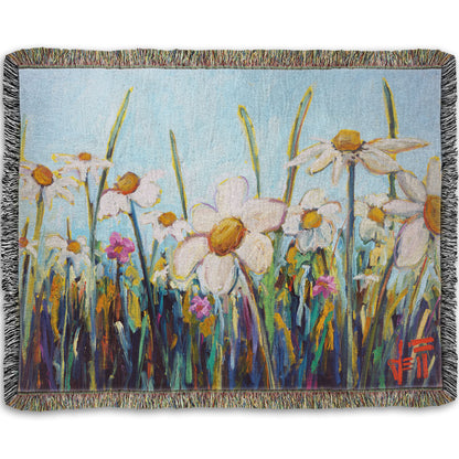 A woven throw blanket designed with a painting of a wildflower field from a low angle, full of white daisies accented by small pink flowers.