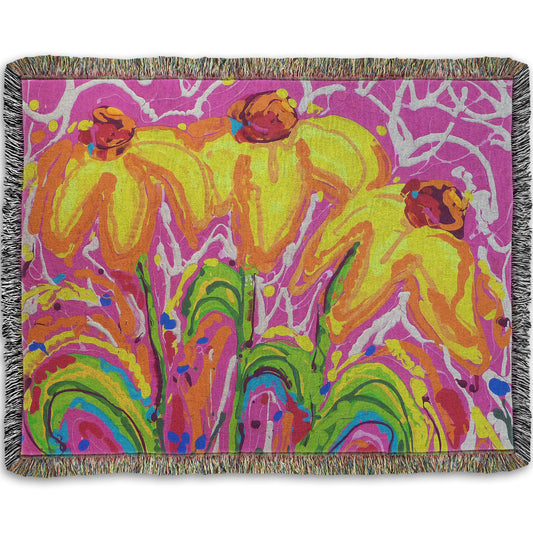A woven blanket designed with a drip painting of three yellow wildflowers on a pink background, accented by orange, blue, green, and white.